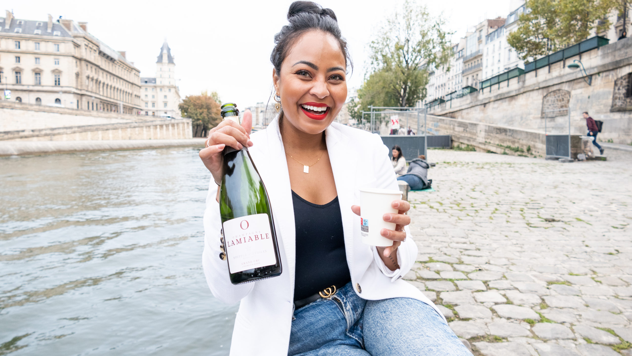 Blogger, Jess of Scotch and the Fox seated along the Seine with a bottle of champagne